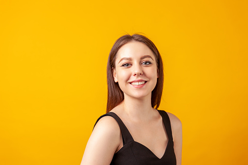 Close-up studio portrait of a cheerful young white woman with brown hair against a yellow background