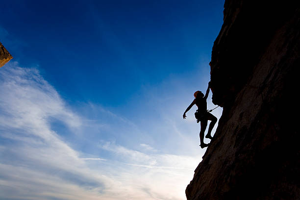 Rock climber clinging to cliff with blue skies in background