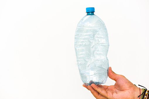 This is a close up photograph of the hand of a man holding an empty plastic water bottle.