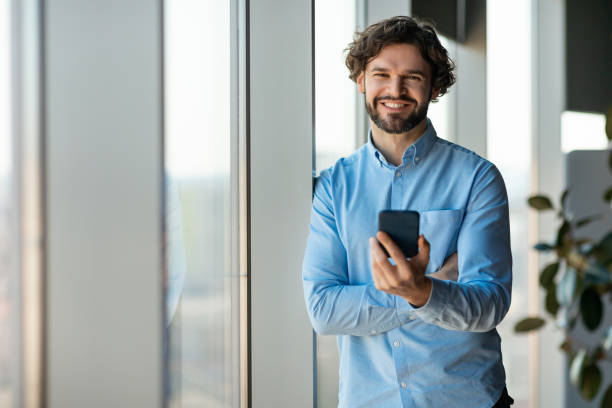 istock Happy mature enterpreneur browsing internet on smartphone, standing near big window in modern office, copy space 1472661401