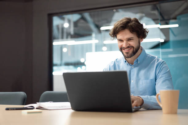 istock Smiling businessman using laptop sitting at desk in office 1472661529