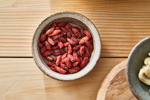 Goji for food preparation, cooking, served on a ceramic plate,  on a wooden kitchen or restaurant table, with fresh and dry seasoning, herbs and spices, representing gourmet indulgence and healthy lifestyle and city life, table top view with a copy space