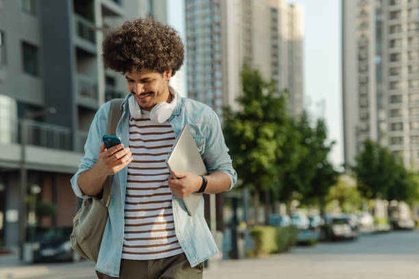 istock Young man looking at phone while carrying laptop 1472663161