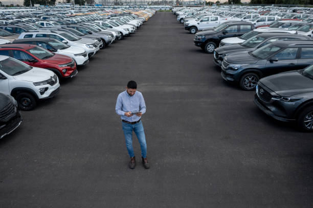 Salesman using a tablet while surrounded by cars at the dealership
