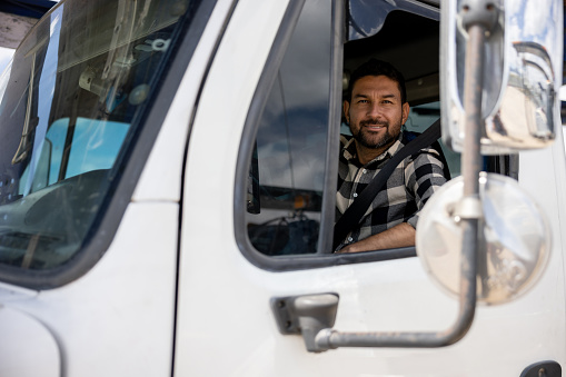 Happy truck driver driving his cargo vehicle and looking at the camera smiling - freight transportation concepts