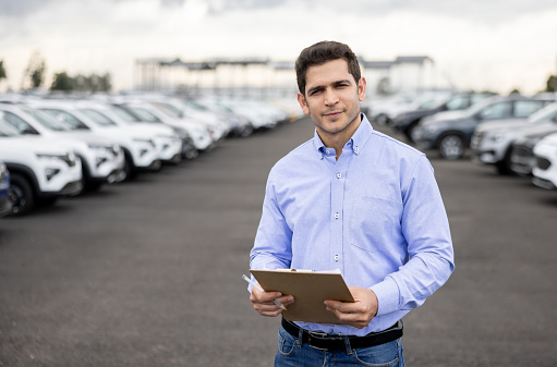 Portrait of a Latin American salesman using a tablet at a car dealership - automobile industry concepts