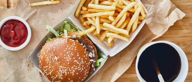 Fresh tasty hamburger with French fries Fresh, tasty and delicious hamburger with French fries on a recycling paper, with ketchup and cola, served on a bamboo wooden cutting board, bar, restaurant or home kitchen table, top view with copy space, representing fast food and city life fast food stock pictures, royalty-free photos & images
