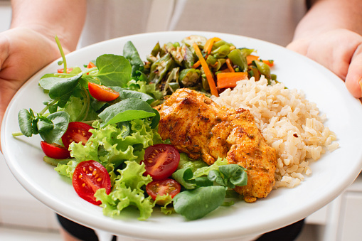 Healthy Meal with Grilled Chicken, Rice, Salad, and Vegetables Served by Woman