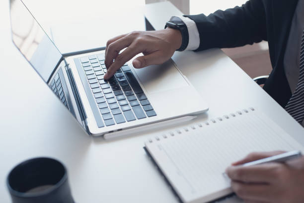 istock Businessman working on laptop computer and writing on notebook on desk at office. Business man planning his work on notepad on office table 1472689397