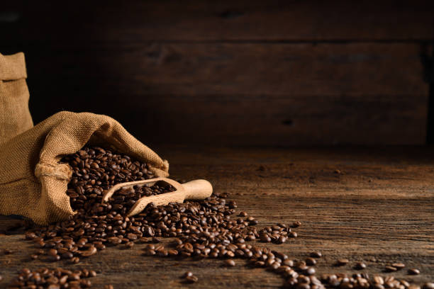chicchi di caffè tostati in sacco di tela sul tavolo di legno - coffee bag coffee bean bean foto e immagini stock