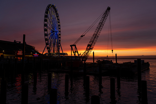 Seattle, USA - Feb 12th, 2023: A vivid sunset over Elliott Bay with The Great Seattle Wheel and new pier construction the waterfront.