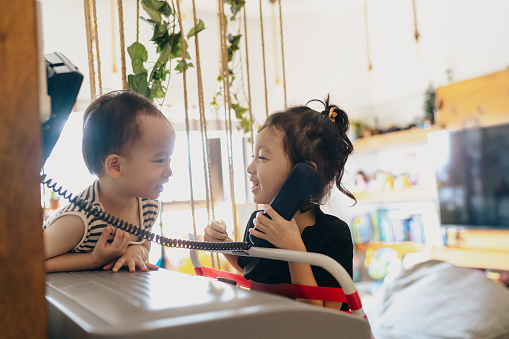 Family bonding and child development - Asian Chinese boy and girl sibling having fun role playing with a traditional landline phone