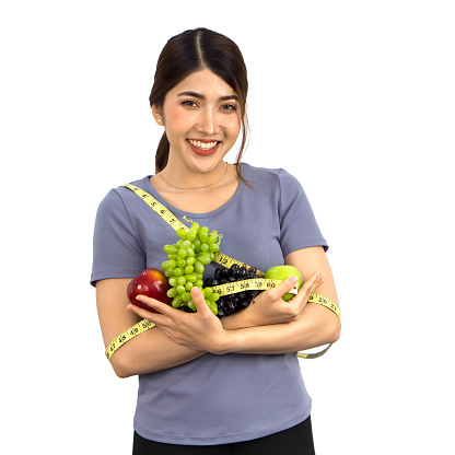 Young asian woman in fitness clothes holding fruits with  measuring tape. Portrait on white background with studio light. Healthy nutrition and weight losing concept.