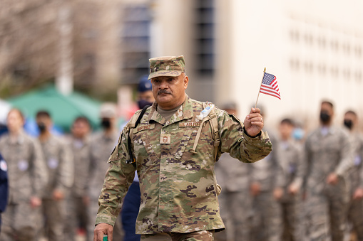 Closeup front view of a cheerful 30's guy holding American flag and looking at the camera.