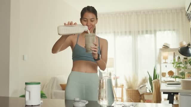 Young Asian athletic woman preparing protein shake at home. Diet and healthy food.