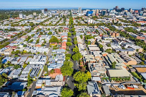 Aerial view of Adelaide CBD from the East side with treelined streets, looking west along Carrington Street to Wright Street over low-rise (low level) residential and business premises to the ocean waters of St Vincent Gulf in distance. Solar panels installed on many rooftops. South Parklands visible in top left of frame.