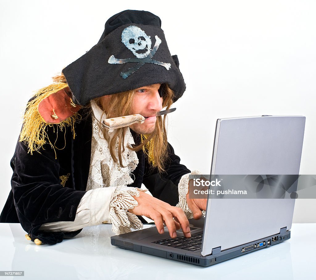 Man dressed as pirate with a knife in his mouth on a laptop pirate attacking with a knife a laptop computer  Pirate - Criminal Stock Photo