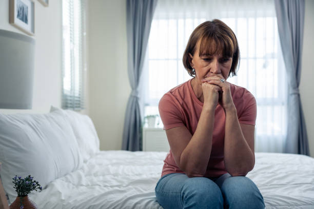 caucasian mature woman frustrating while sit alone on bed in bedroom. attractive old female upset depressed feel infuriating, sad and upset with life problem in house. health care medical concept. - ansiedade imagens e fotografias de stock