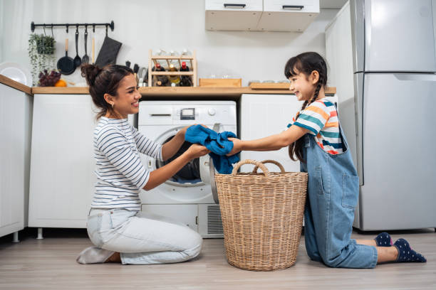 mãe caucasiana bonita ensinando filha pequena lavar roupas sujas. adorável menina menina bonita ajuda e aprender com a mãe dos pais para colocar a roupa no aparelho de lavar em casa. doméstica-housekeeping. - stereotypical housewife little girls family domestic kitchen - fotografias e filmes do acervo