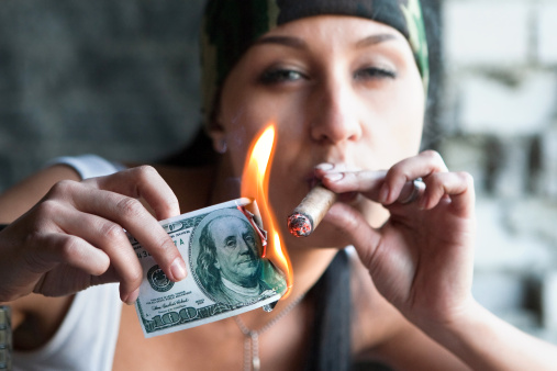 Pretty girl is lighting a cigar from one hundred dollars bill.