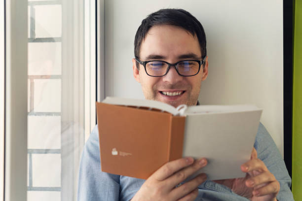 istock young man reading book at home by window 1472738050