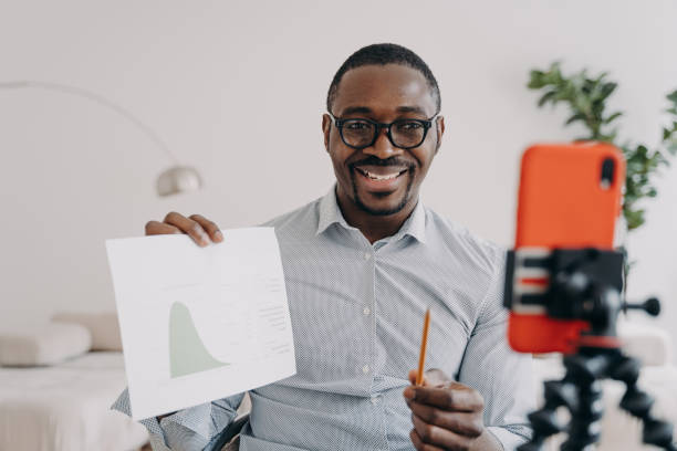 istock Afro freelancer has online brainstorm. Positive man shows data chart speaking at online conference. 1472740986