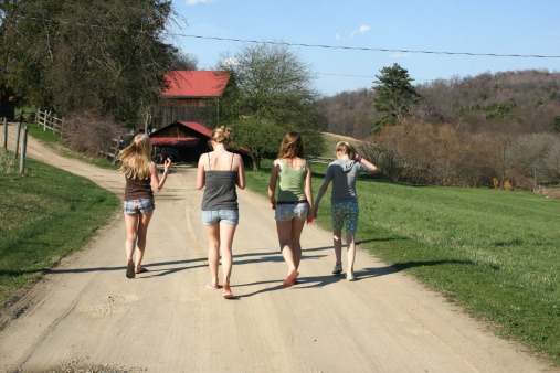 Teenage girls head down a dirt road to the barn on a Pennsylvania farm.