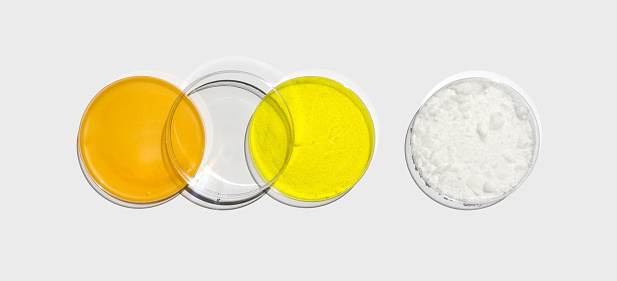 Shower cream, Potassium Chromate powder and Cetyl Esters Wax in petri dish with plastic lid on white laboratory table. Chemical ingredient for cosmetics and toiletries product. Top View