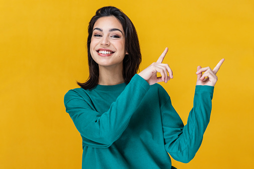 Portrait of beautiful smiling woman pointing up over yellow background.