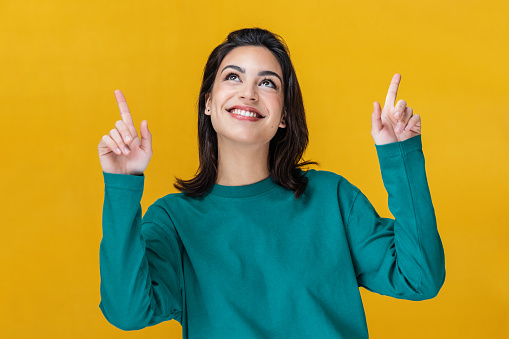 Portrait of beautiful smiling woman pointing up over yellow background.
