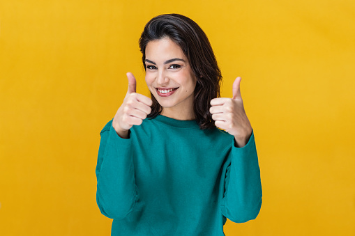 Portrait of beautiful young woman expressing happiness with thumb isolated on yellow
