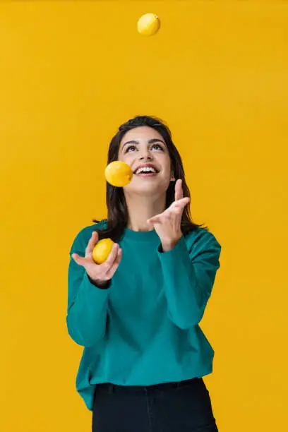 Portrait of a laughing woman juggling lemons isolated on yellow