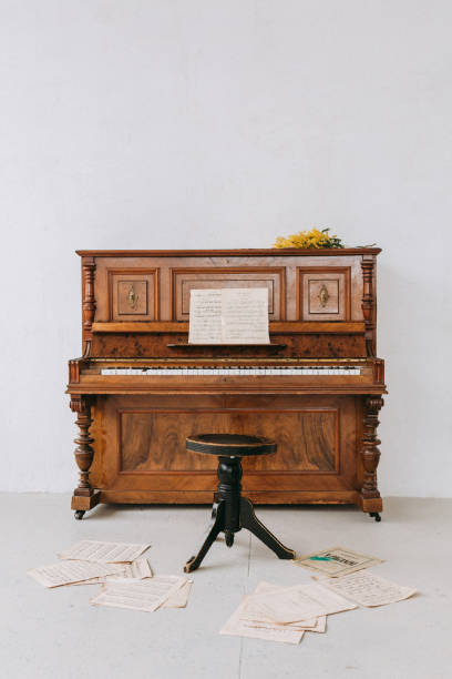 istock Old fashioned piano in a white room with  music notes lying on the floor 1472749910