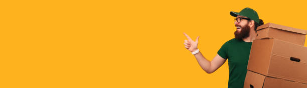 istock Banner size shot of a delivery man holding boxes while pointing aside. 1472750047
