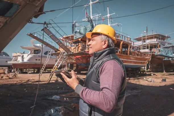 Mature mechanic technician checking motorboats at shipyard