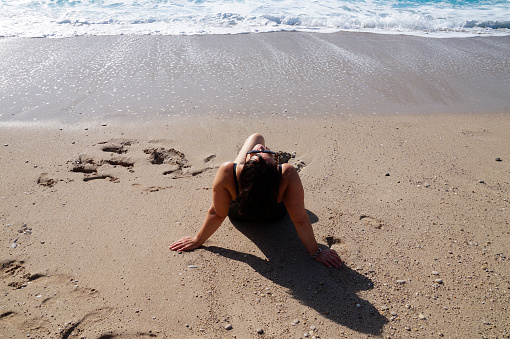 curvy woman sunbathing on the beach with her head thrown back to the sun.