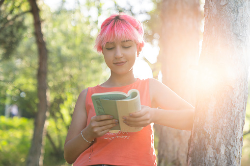 non-binary young woman reading a book in the park