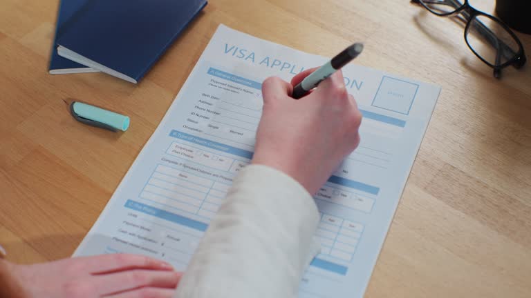 Woman hand filling visa application form on desk. Legal immigration, tourist interview.