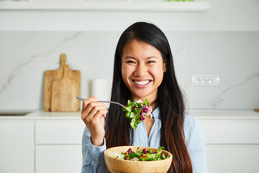 Portrait of a fit healthy asian woman, in the modern home kitchen, preparing vegan food at the dining table who is filled with the fresh organic vegetables, representing a healthy lifestyle, an image with a large copy space area