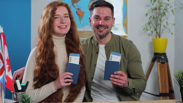 A happy couple shows their tickets and passports, expressing great joy because they got the chance to spend their summer vacation abroad. Travelling concept.