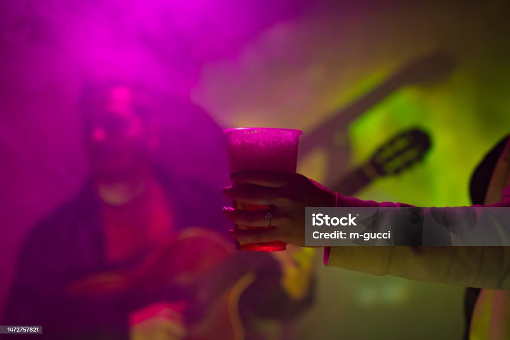 Nő műanyag söröspoharat tart a kezében, a klub hátterében gitározó zenésszel. - Jogdíjmentes Ale témájú stock fotó Nő műanyag söröspoharat tart a kezében, a klub hátterében gitározó zenésszel. - Jogdíjmentes Ale témájú stock fotó