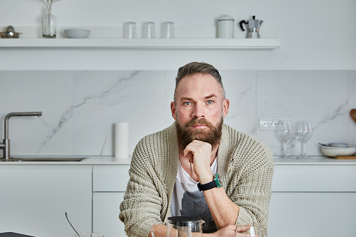 Portrait of a fit and beautiful white man with a beard, sitting in the modern home kitchen, preparing breakfast at the dining table, herbal tea, croissants and the freshest organic fruit, avocado and banana, representing a healthy lifestyle, an image with a large copy space area