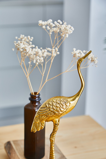 Dry flowers in a glass bottle and a golden crane sculpture, on a kitchen wooden table, representing zen-like mood atmosphere