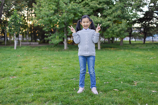 Portrait of charming little girl 9-11 years, looking at camera and pointing fingers down, standing in casual pink t shirt over wooden background