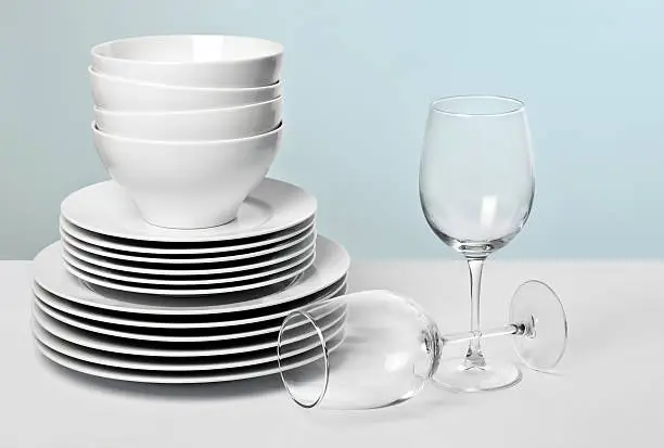 Stack of commercial plates and bowls on table beside two wine glasses