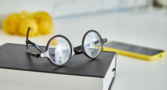 Eyeglasses on a book at cozy modern home kitchen, with a smart phone in the back, representing a healthy lifestyle, wellbeing and mind and body care