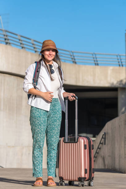istock Female traveler smiling while standing outdoors with a suitcase. 1472761517