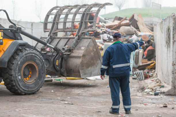 istock Landfill worker directing skid steer loader on the waste heap, rear view 1472761777