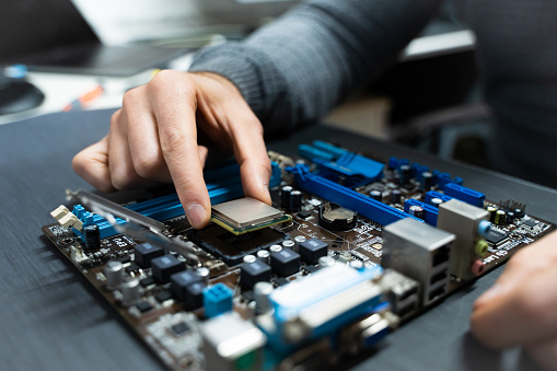 A man's hand picking up a cpu from a damaged computer motherboard.