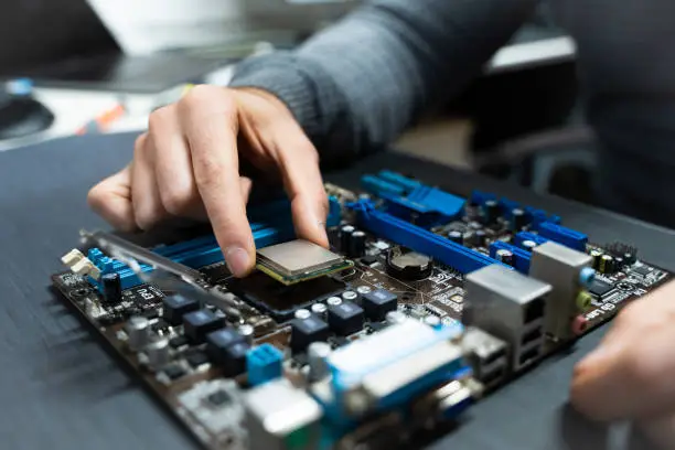 Photo of A man's hand picking up a cpu from a damaged computer motherboard.